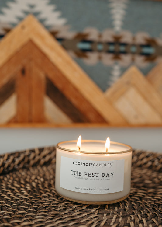 The Best Day Candle from Footnote Candles. Mini candle is sitting on woven wood tray, with wood accent piece behind it.