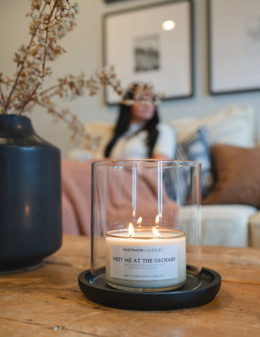 Glass Hurricane and Black Wood Tray from Footnote Candles. On living room coffee table, with woman reading.