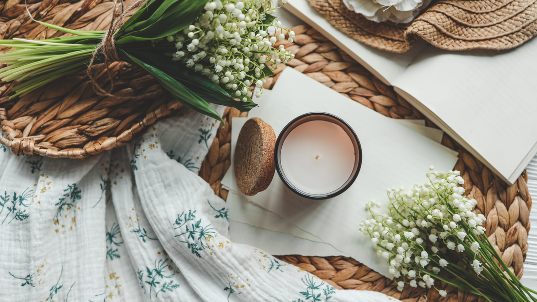 Photo of light color floral print fabric with woven rattan tray sitting on top, accented with fresh spring floral sprigs and candle in amber glass vessel